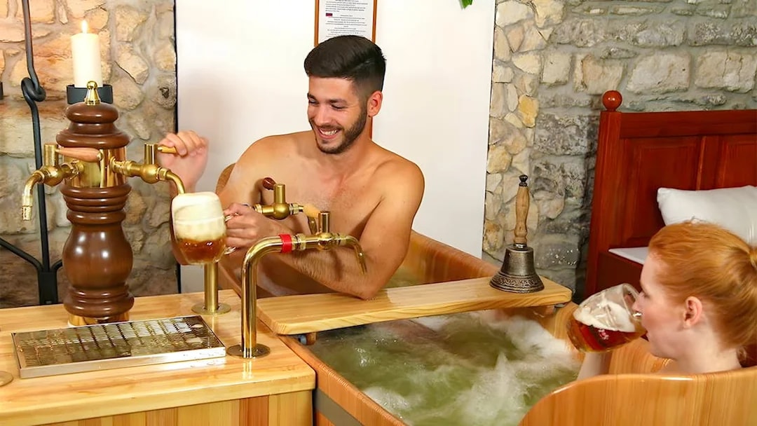 Couple enjoying a beer bath at Bernard Beer Spa with wooden tubs and beer taps.