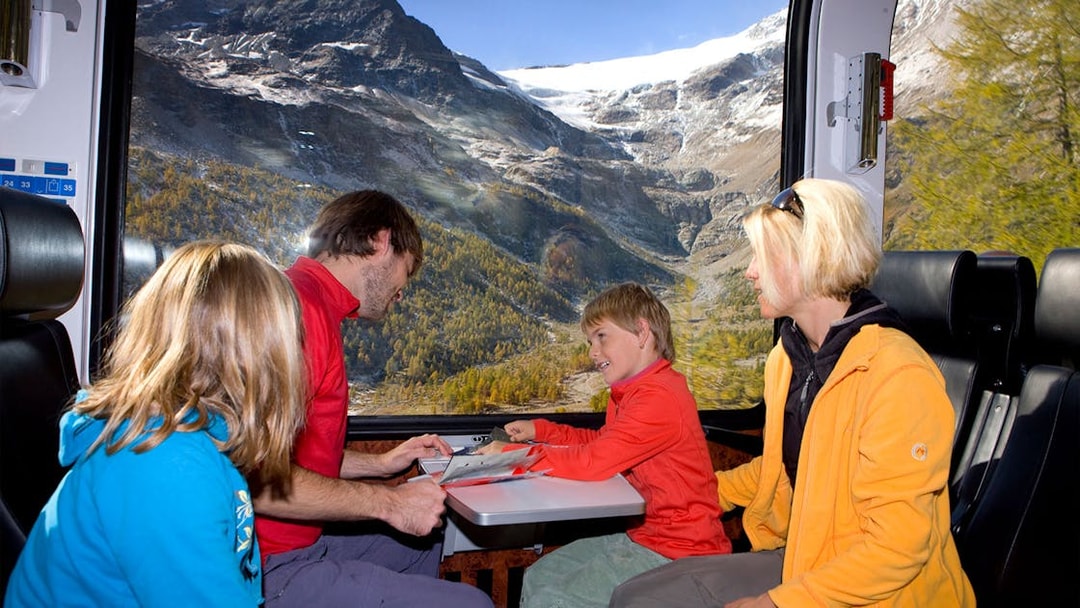 Family enjoying Bernina Express train ride through snowy St Moritz Alps.