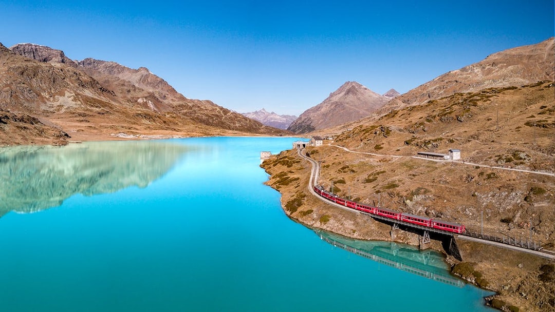Bernina Express train crossing a bridge over a turquoise lake in the Swiss Alps.
