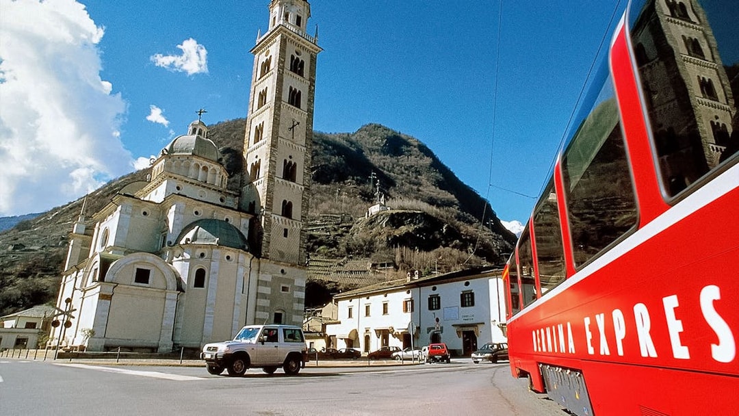 Bernina Express train passing by a historic church in Tirano, Italy.