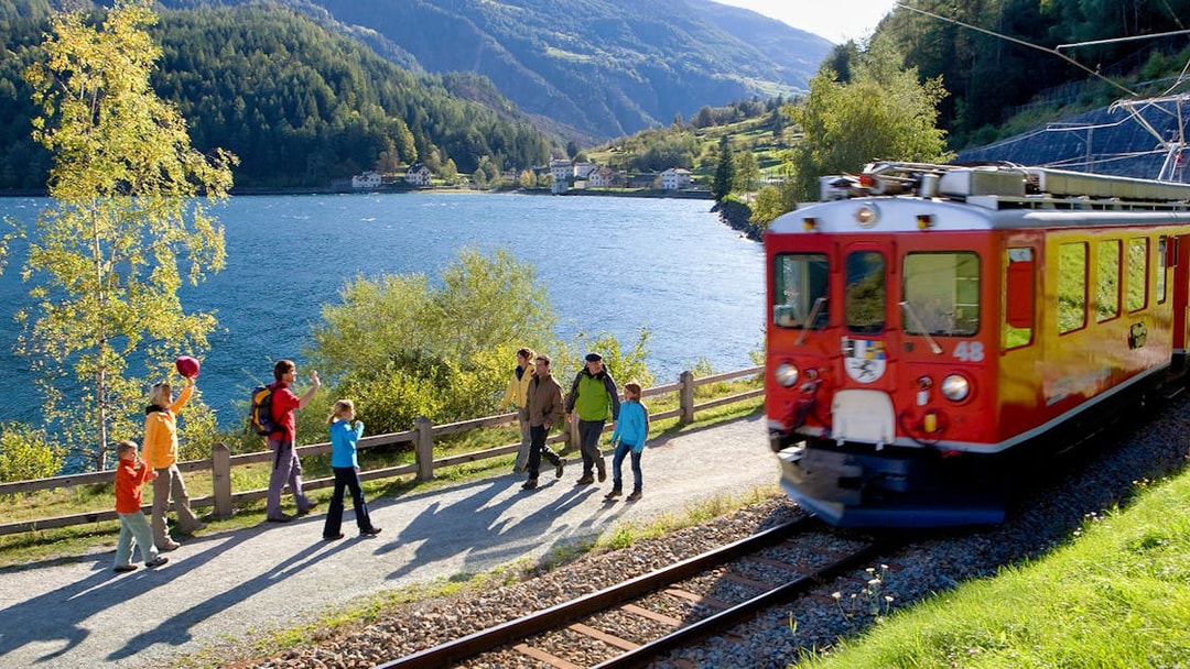 Bernina Express train passing by hikers near a lake in the Swiss Alps, close to St. Moritz.