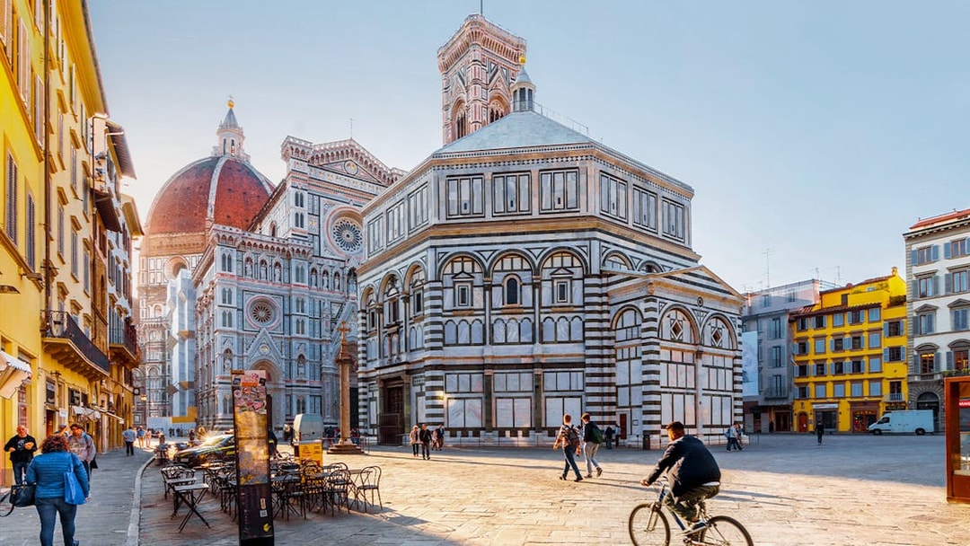 Baptistery and Florence Cathedral in Piazza del Duomo, Florence, with people walking and cycling.