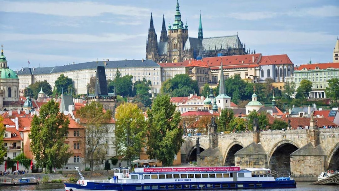 Panoramic view of Prague Castle and Charles Bridge with a cruise boat on the Vltava River.