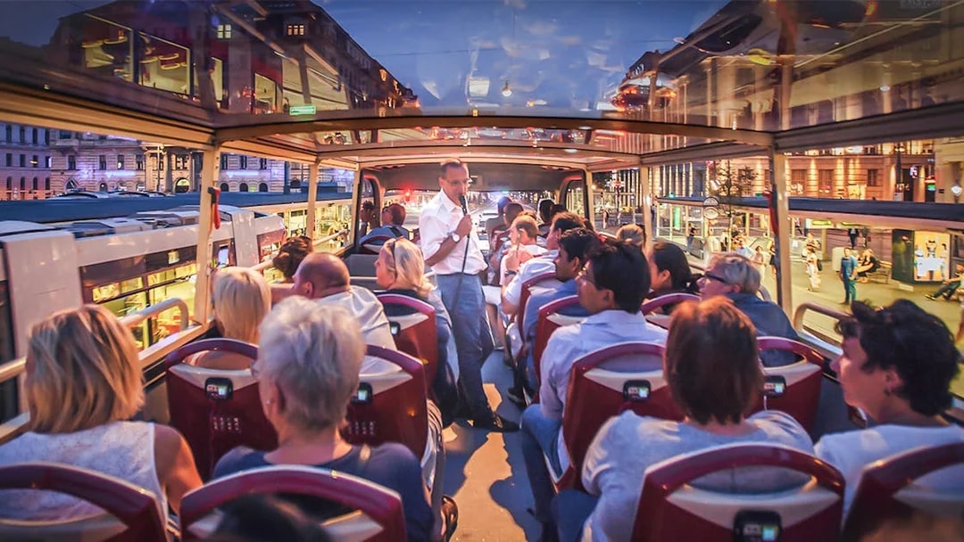 Open-top bus tour in Berlin at night with passengers and guide.