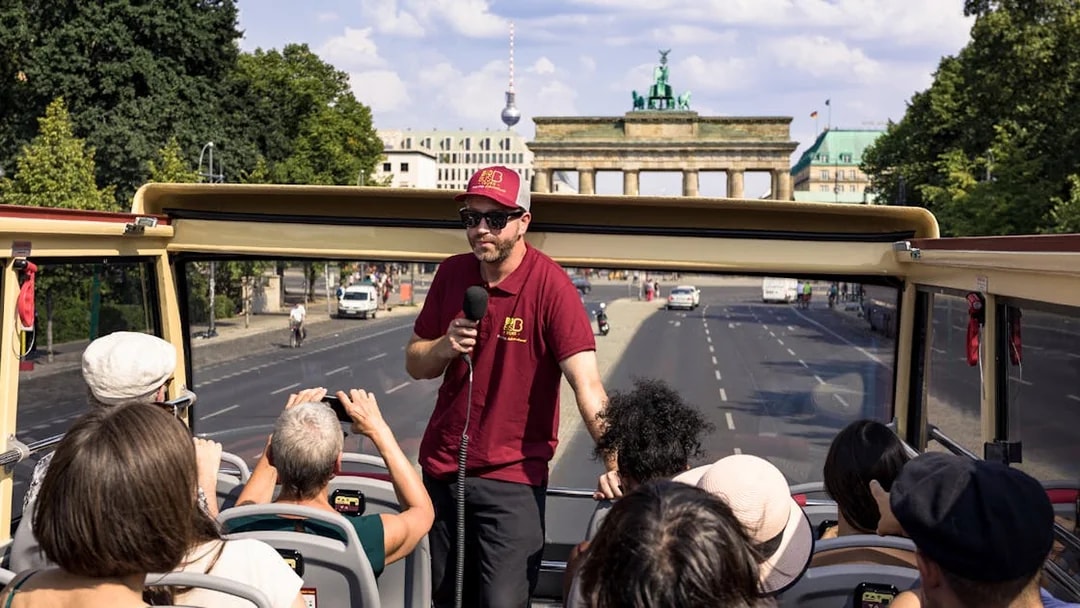 Guide speaking to tourists on Bigbus HOHO Berlin with Brandenburg Gate in view.