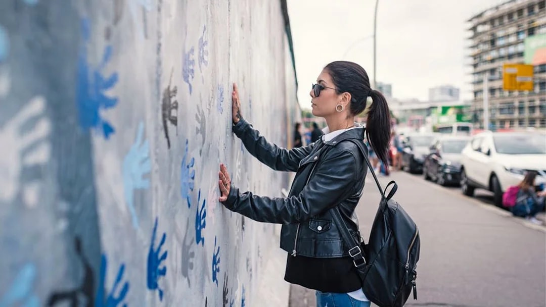 Woman viewing handprint graffiti on Berlin Wall.