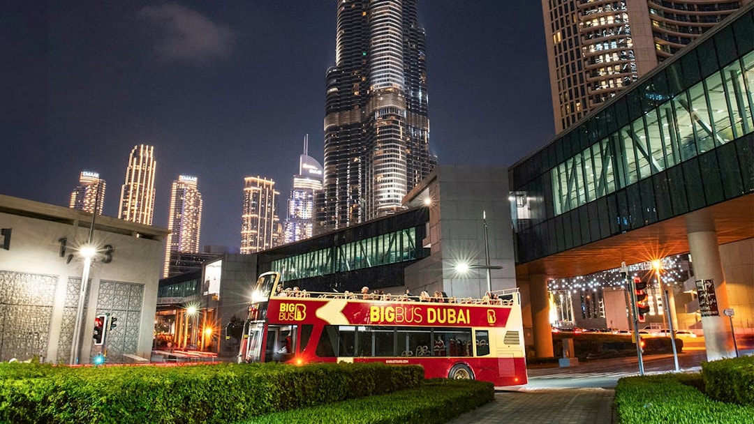 Big Bus Dubai night tour passing by illuminated skyscrapers.