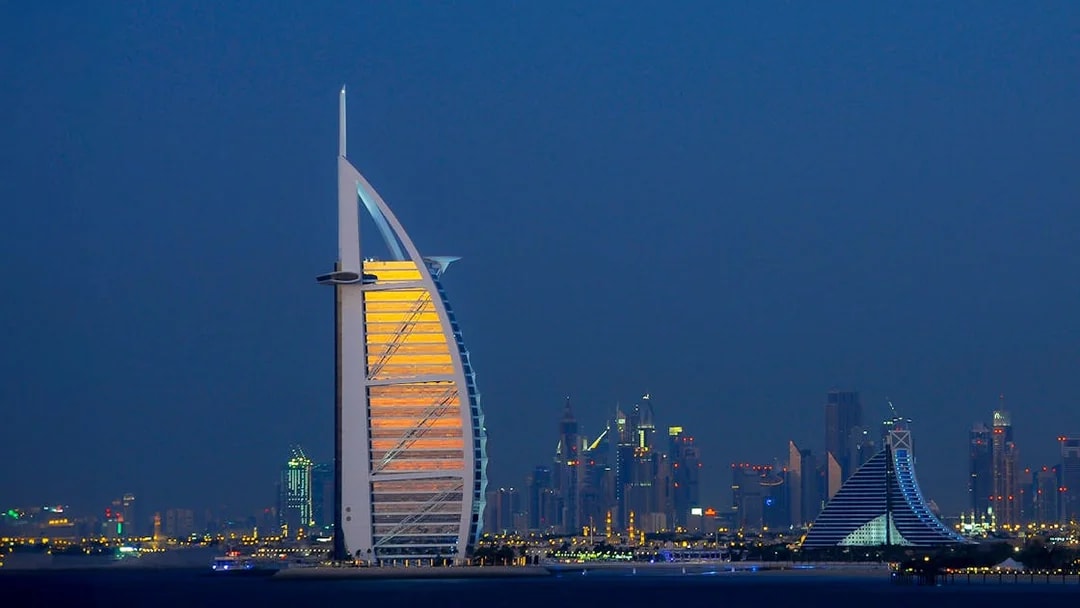 Burj Al Arab illuminated at night with Dubai skyline in the background.