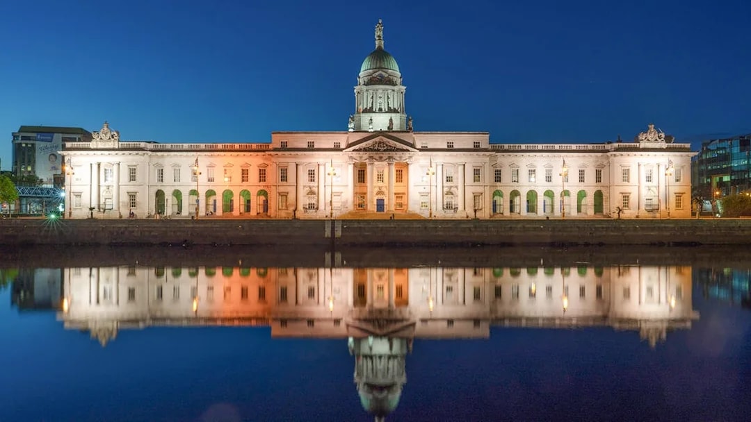 Parliament House in Dublin illuminated at night, reflecting in the river.