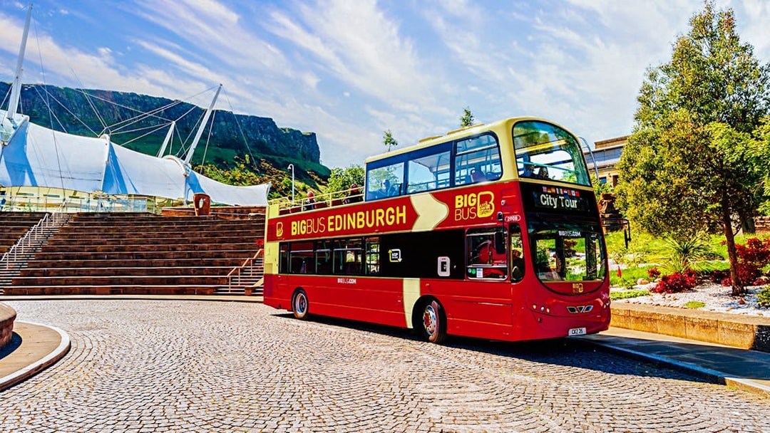 Edinburgh hop-on hop-off bus near modern architecture and Arthur's Seat.