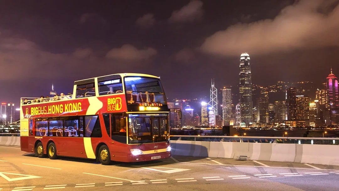 Hop-on-hop-off bus in Hong Kong with city skyline at night.