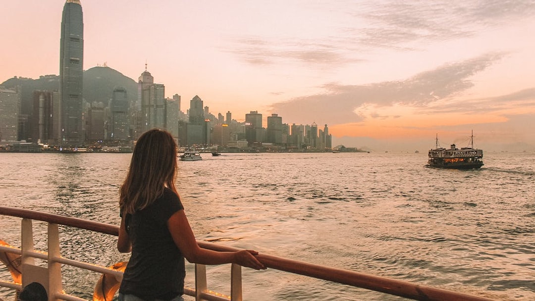 Hong Kong skyline at sunset viewed from a ferry, with a woman looking out over the water.