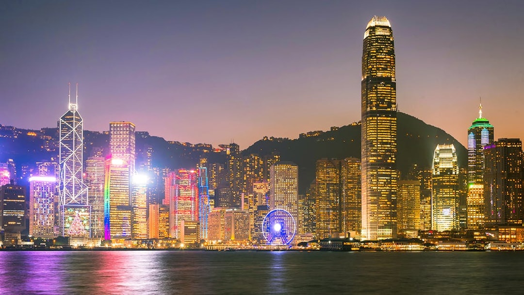 Hong Kong skyline at night with illuminated skyscrapers and Ferris wheel.