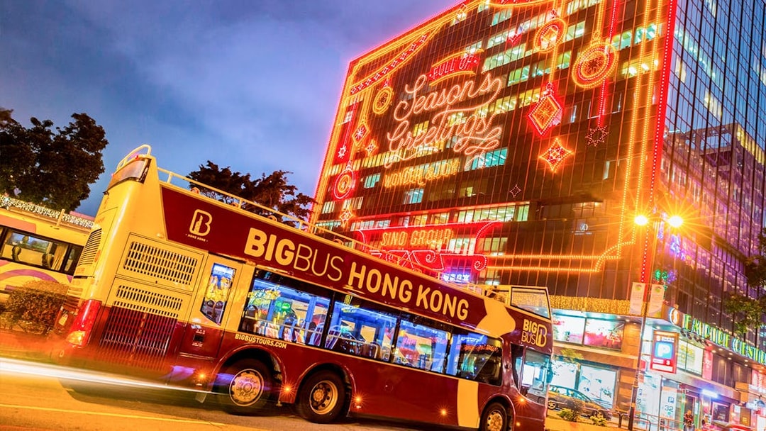 Hop-on-hop-off bus in Hong Kong with festive lights on a building.
