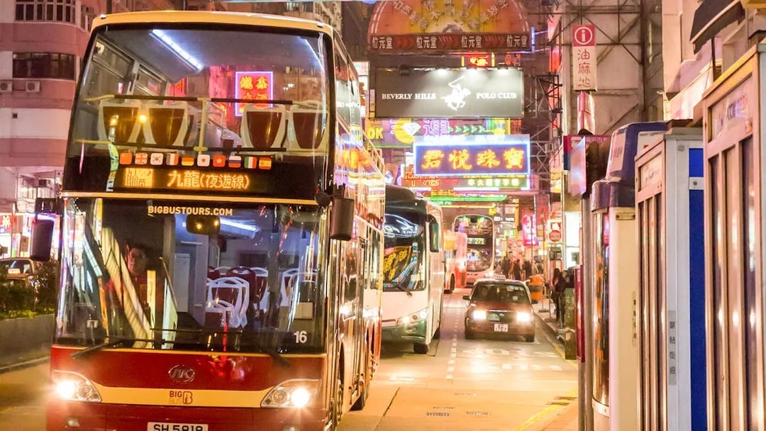 Hop-on-hop-off bus on a vibrant street in Hong Kong at night.
