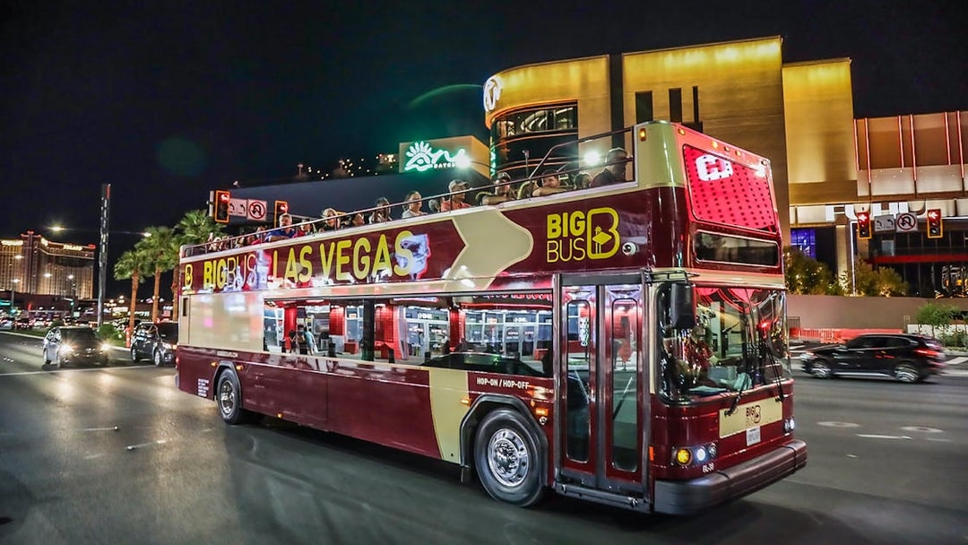 Big Bus tour in Las Vegas at night with passengers on upper deck.