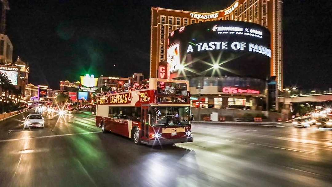 Big Bus tour driving on Las Vegas Strip at night near Treasure Island.