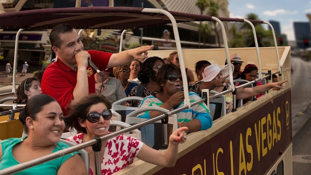 Tourists on Las Vegas hop-on hop-off bus pointing at attractions.