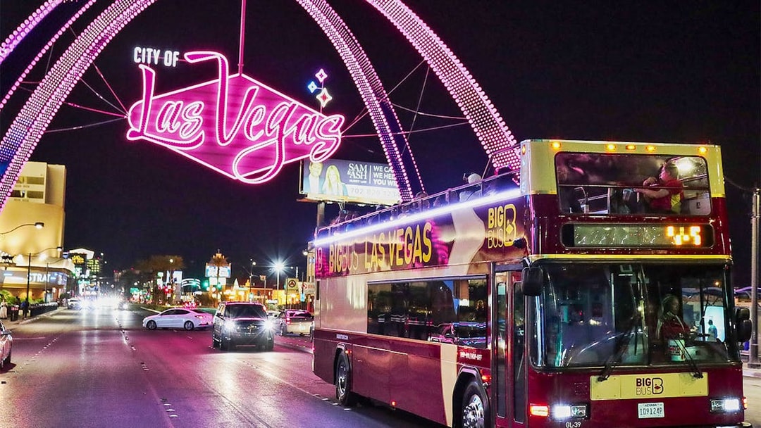 Big Bus tour in Las Vegas at night under neon city sign.