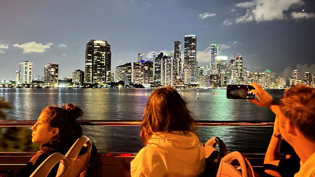 Passengers on Big Bus Miami Night Tour viewing illuminated Miami skyline.