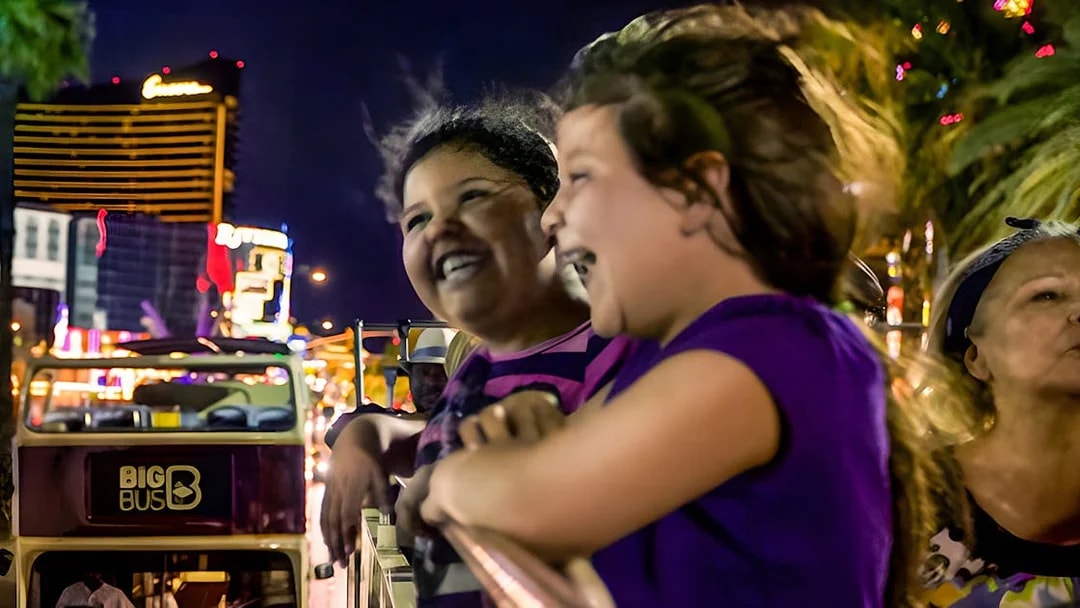 Open-top bus tour at night in Miami with people enjoying city lights.
