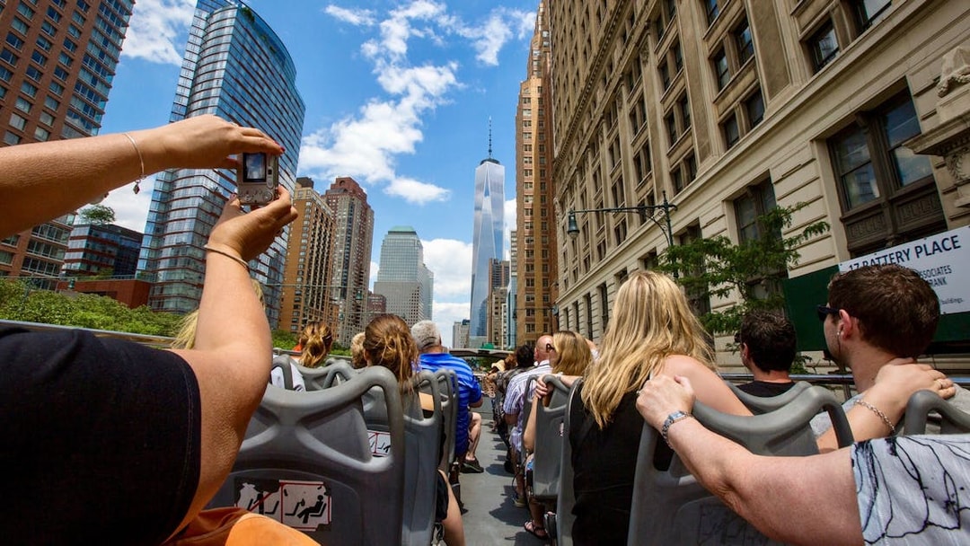 Open-top bus tour in New York City with view of skyscrapers and tourists.