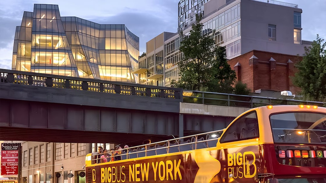 Big Bus New York night tour passing under illuminated modern architecture.
