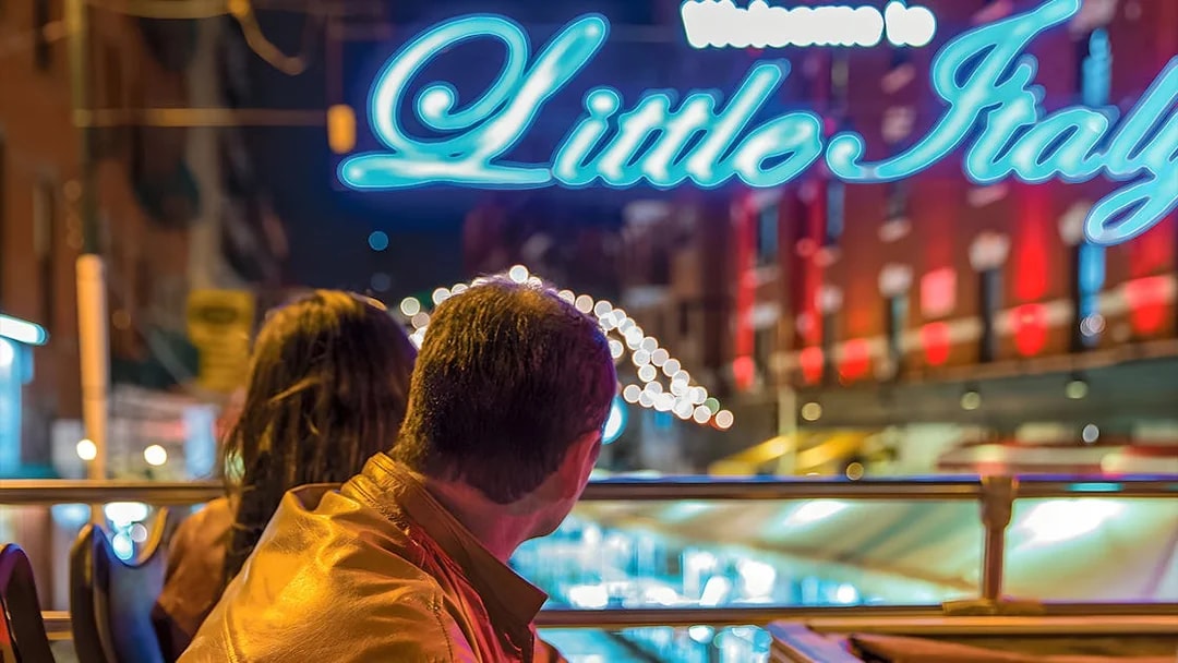 Couple on Big Bus tour viewing Little Italy sign in New York at night.
