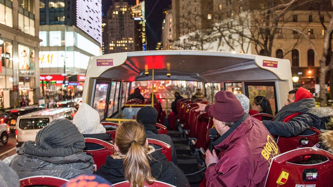 Passengers on a Big Bus night tour in New York City, viewing illuminated skyscrapers.