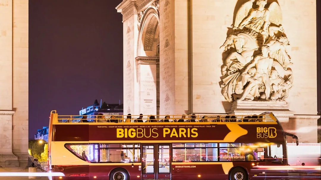 Big Bus tour passing by the Arc de Triomphe at night in Paris.