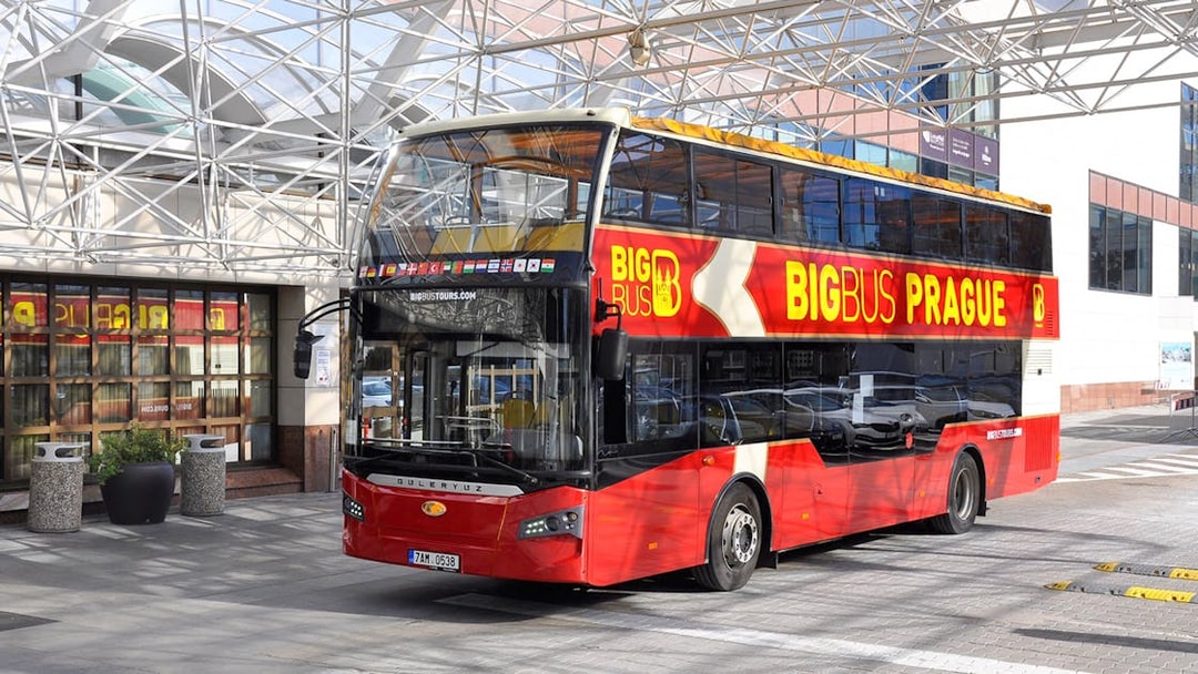 Red double-decker bus for Prague hop-on hop-off tour parked under a glass canopy.
