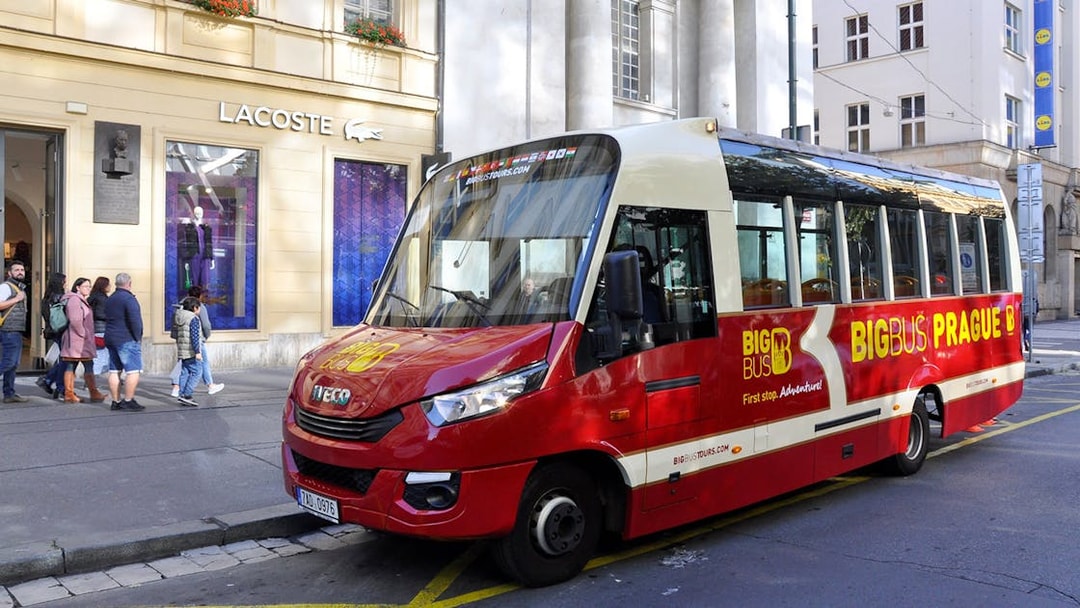 Red Big Bus tour vehicle parked in Prague city center near Lacoste store.