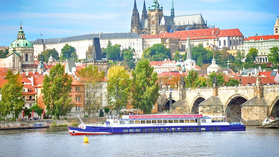 Cruise boat on Vltava River with Prague Castle and Charles Bridge in the background.