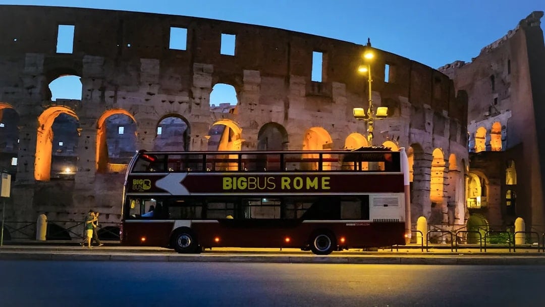 Big Bus tour in front of the Colosseum, Rome, at dusk.