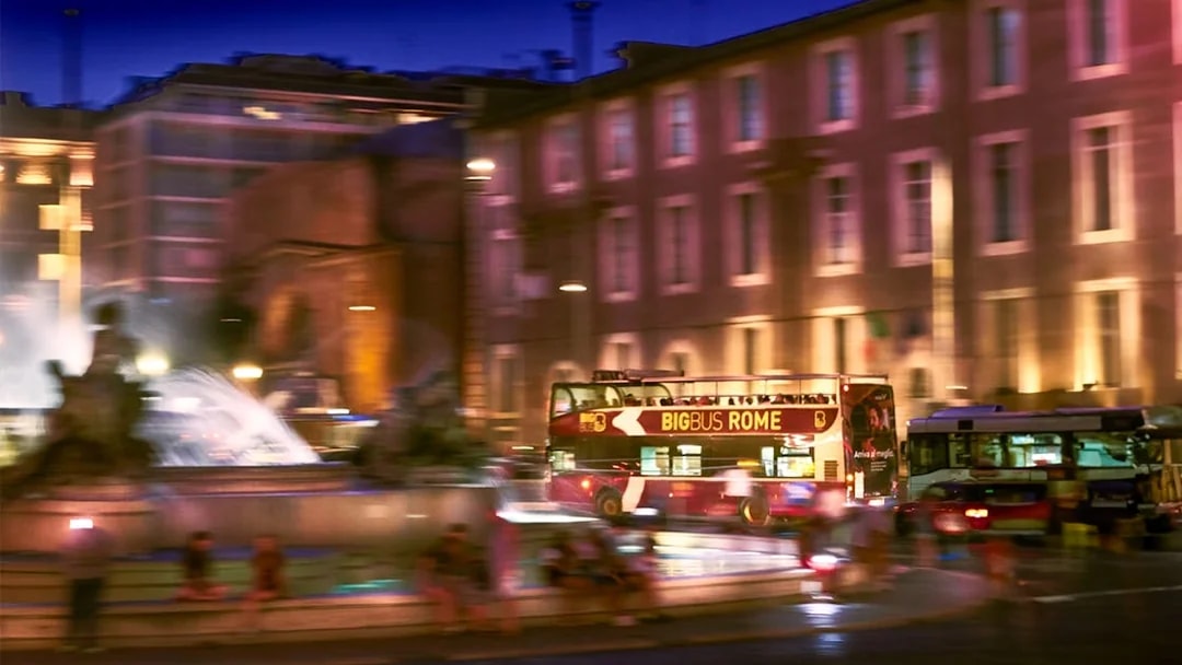 Big Bus tour passing by a fountain in Rome at night.