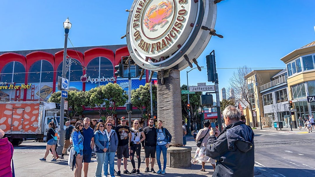 Tourist photographing group near Fisherman’s Wharf sign, San Francisco.