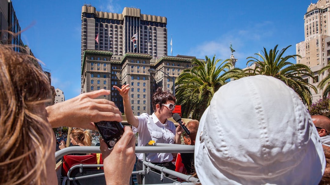 Tour guide speaking on a Big Bus in San Francisco with city buildings in the background.