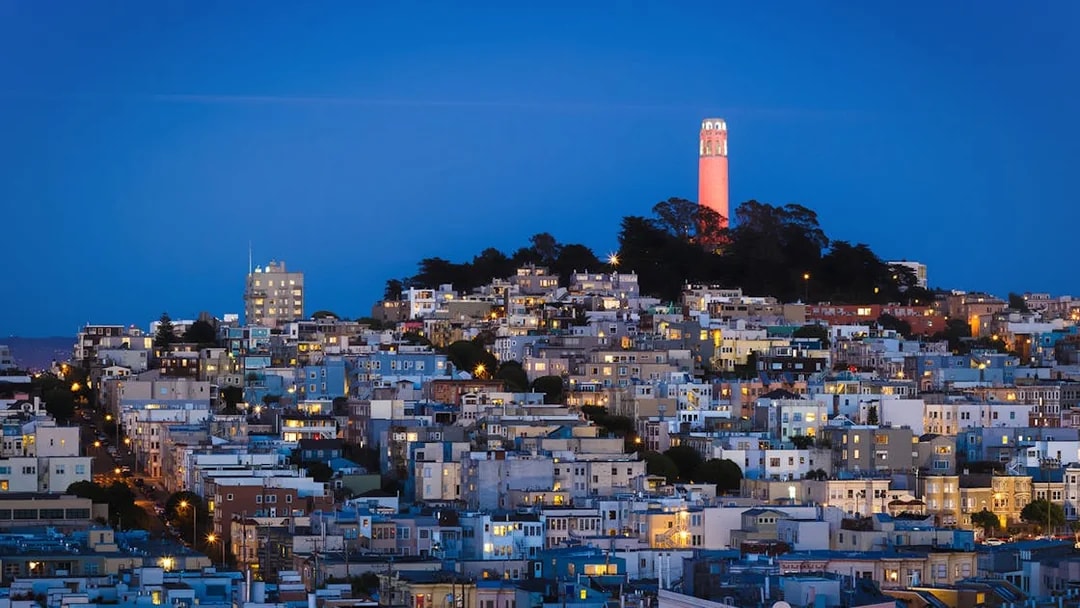 San Francisco skyline with Coit Tower illuminated at sunset.