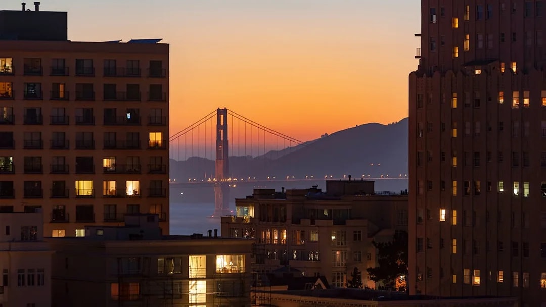 Golden Gate Bridge at sunset viewed between city buildings.