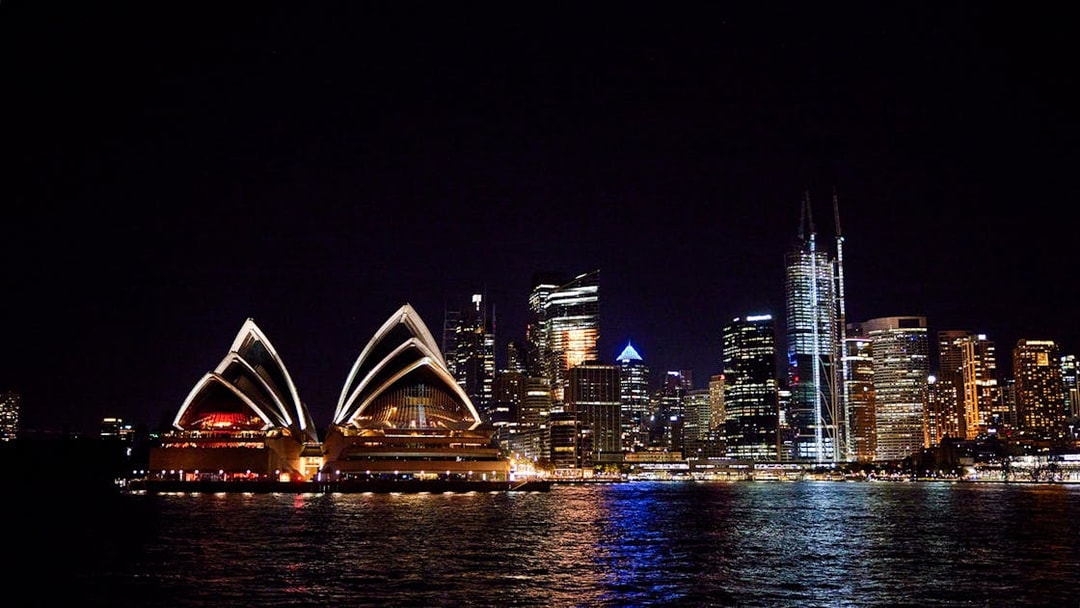Sydney Opera House and city skyline at night with reflections on the water.