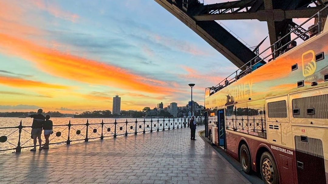 Big bus parked near Sydney Harbour at sunset.
