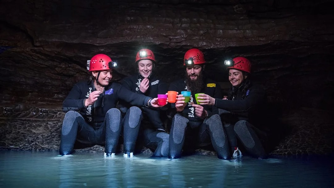 Group enjoying Black Water Rafting in Waitomo cave, wearing helmets and wetsuits.