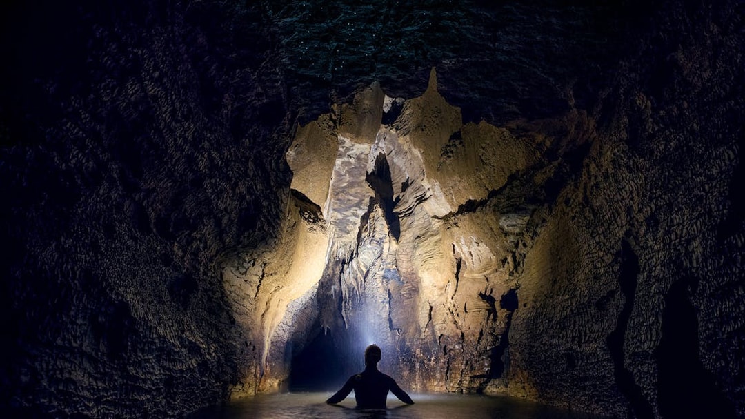 Person exploring illuminated cave during black water rafting in Waitomo.