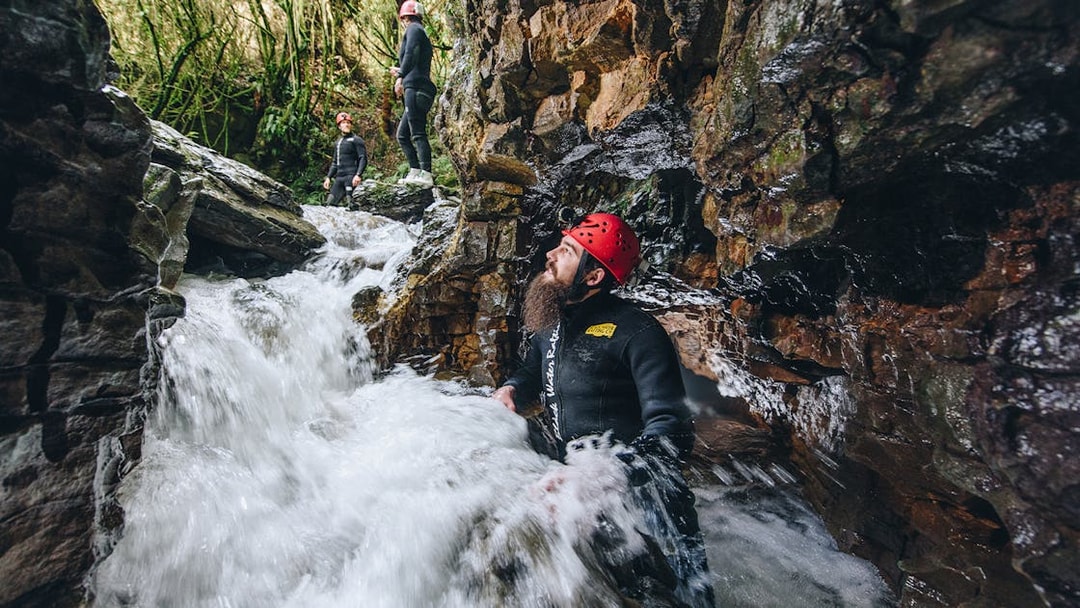 Adventurers in wetsuits and helmets navigate rocky stream in Waitomo cave.