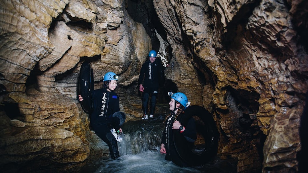 Adventurers in wetsuits and helmets explore a cave during a black water rafting tour in Waitomo.