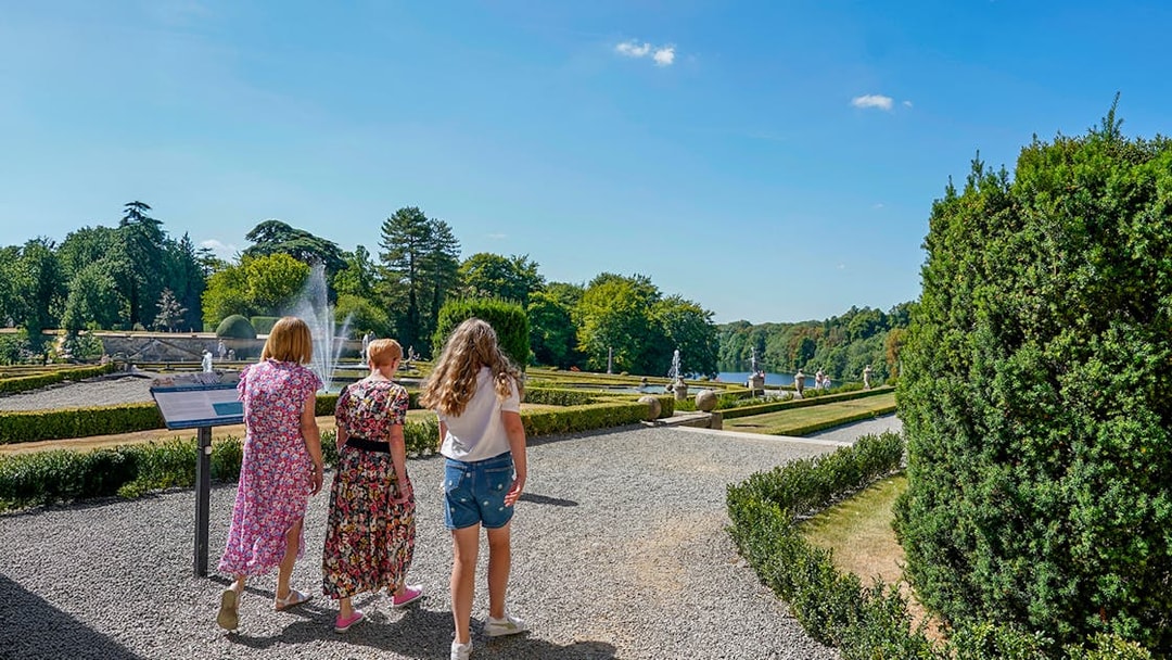 Visitors walking through palace gardens with fountains and manicured hedges.