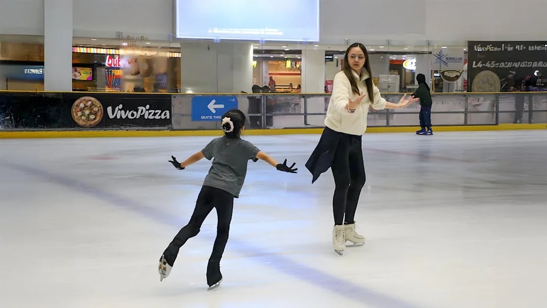 Coach guiding girl on ice at Blue Ice Snow Park, Johor Bahru.