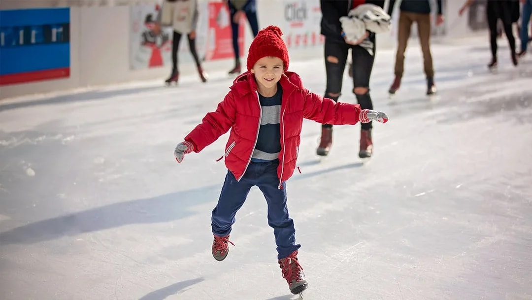 Young boy ice skating on a rink wearing a red jacket and hat.