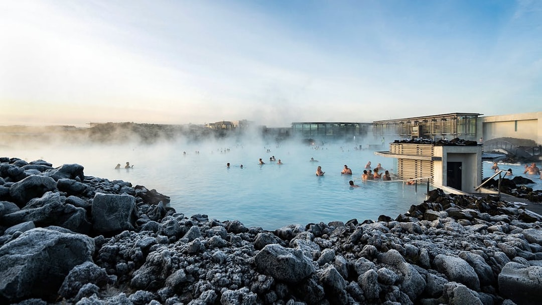 People enjoying the Blue Lagoon geothermal pool surrounded by rocky landscape in Iceland.