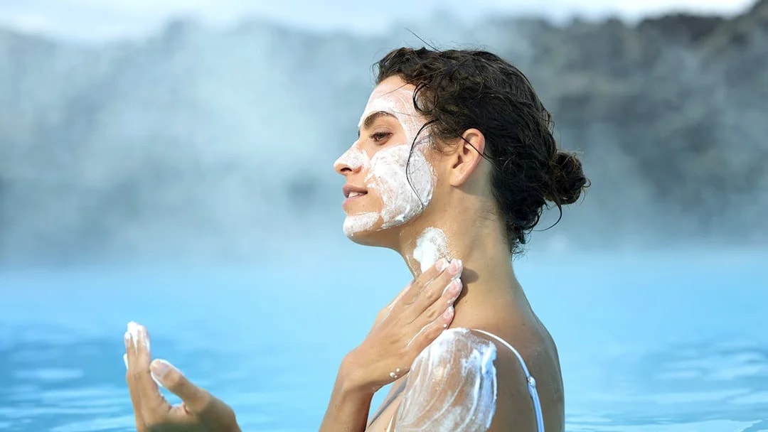 Tourist applying mud mask at Blue Lagoon geothermal pool in Iceland.